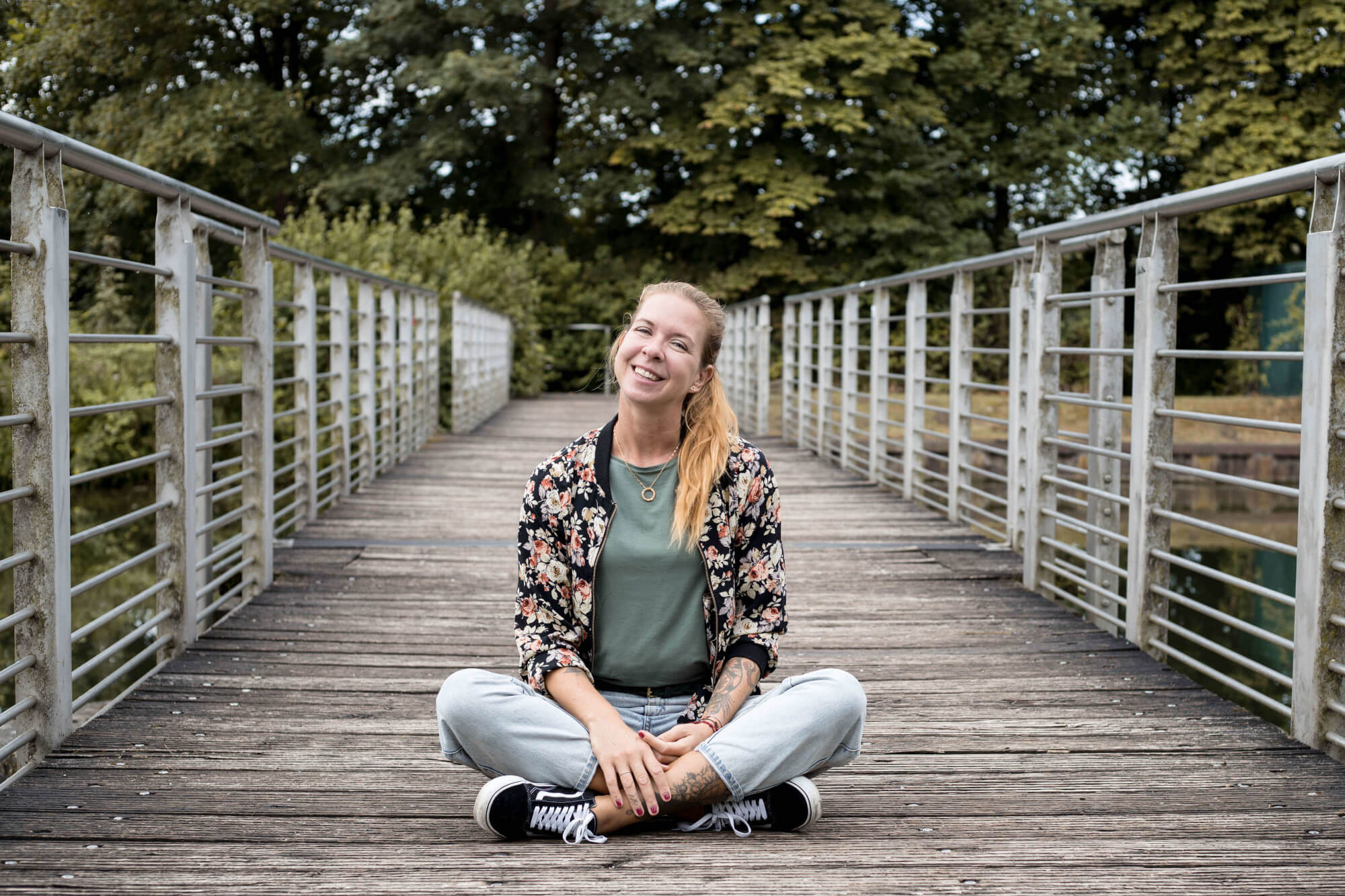 Irena, Onlinemarketingexpertin für Tierunternehmer sitzt im Schneidersitz auf einer Holzbrücke. 